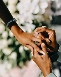 two people holding hands over each other with flowers in the backgroung behind them