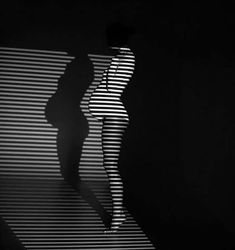 a woman is standing in the dark with her shadow on the wall behind her,