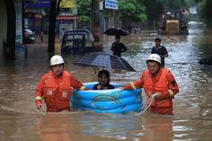 three people in orange jackets and white hats are holding an umbrella while standing in a flooded street