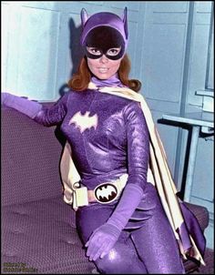 a woman dressed as batgirl sitting on top of a couch with her arms outstretched