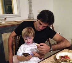 a man sitting at a table with a little boy on his lap looking at a cell phone