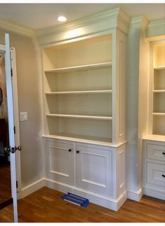 an empty room with white bookcases and wooden floors