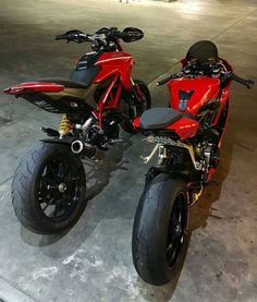 two red motorcycles parked next to each other in a parking lot with concrete flooring