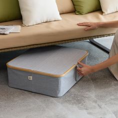 a woman sitting on the floor next to a couch with a storage box underneath it