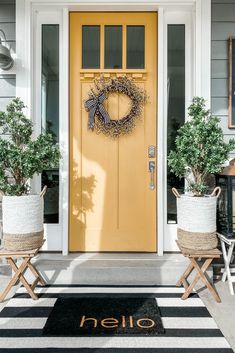 a yellow front door with two planters and a welcome mat