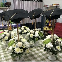 four graduation hats are placed on top of flowers in vases at a table with green and white checkered cloth