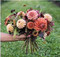 a bouquet of flowers being held by someone's hand on the grass in front of them