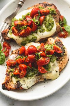 two pieces of chicken covered in pesto and cherry tomatoes on a plate with a fork