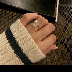 a woman's hand with a diamond ring on her finger, next to a black table