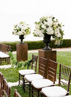 there are many chairs and vases with flowers in them on the grass near each other