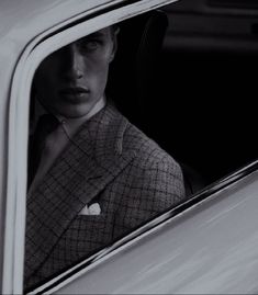 a man wearing a suit and tie sitting in a car looking out the window at something