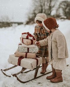 two children pulling a sleigh with presents on it in the snow and one child is wearing a hat