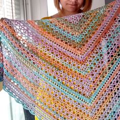 a woman holding up a multicolored crocheted shawl