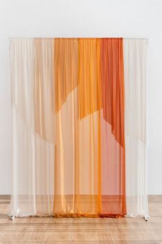 an orange and white curtain is hanging on the side of a wall in front of a wooden floor