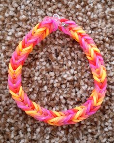 a pink, yellow and orange braided bracelet sitting on top of a brown carpet