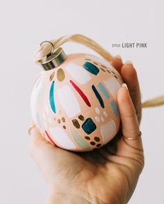 a hand holding a painted ornament in front of a white background with the words shine light pink on it