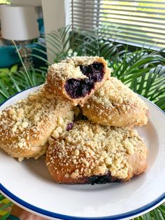 three blueberry crumbs sitting on top of a white plate next to a window