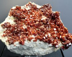 a rock with red and white crystals on it sitting on a black stand in front of a gray background