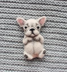 a small white dog sitting on top of a gray knitted blanket with it's eyes closed