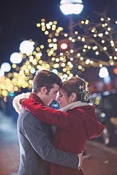 a man and woman embracing each other in front of christmas lights