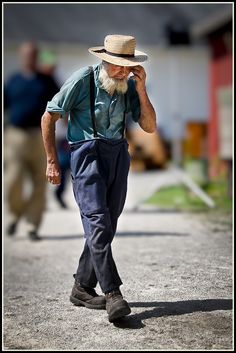 an old man walking down the street talking on his cell phone while wearing a hat