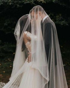 a bride and groom kissing in front of some trees with their veils pulled back