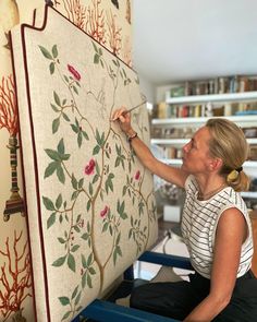 a woman is working on a wall hanging