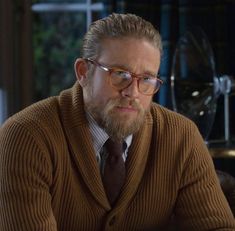 a man wearing glasses and a sweater sits at a table