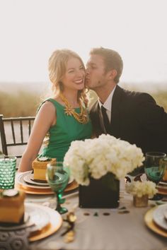 a man and woman sitting at a table with plates, cups and vases on it