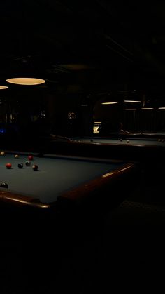 two pool tables in a dark room with lights hanging from the ceiling and several billiards