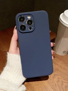 a person holding up a blue phone case next to a cup of coffee on a wooden table