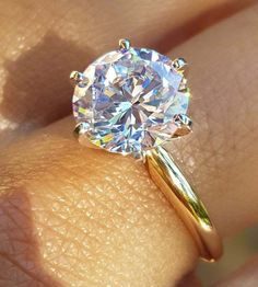 a woman's hand holding a diamond ring on her finger, with the center stone in