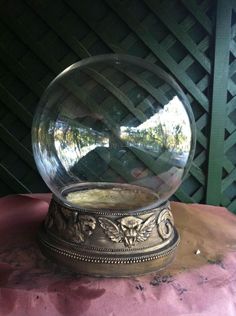 a glass ball sitting on top of a pink cloth covered table next to a green fence