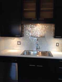 a kitchen with black cabinets and a silver sink in the center, under a mosaic tile backsplash