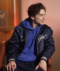 a young man sitting in a chair wearing a blue hoodie and looking off to the side