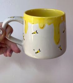 a hand holding a yellow and white coffee mug with bees painted on the side,