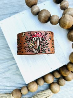 a wooden bead necklace with a leather bracelet on top of it and a mushroom painted on the clasp