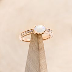 an opal and diamond ring sits on top of a wooden stand in front of a beige background