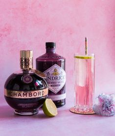 two bottles of alcohol next to a glass with a lime slice on it and a pink background