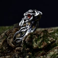 a silver ring with a red stone in the center on top of mossy rocks