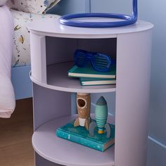 a white shelf with books and toys on it in a bedroom area next to a bed