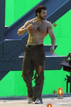 a shirtless man standing in front of a green screen with his hand on his hip