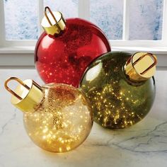 three christmas ornaments sitting on top of a marble counter next to a window with snowflakes