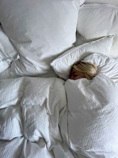 a woman laying in bed with white sheets and pillows