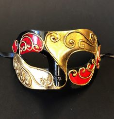 This Venetian Men's Eye Mask has a unique look and is hand painted red, black, gold and silver with a raised detail. Mask and comes with black silk ribbon ties attached. This mask is great for Masquerade and Venetian Mask Parties! Size 7"W x 4"H Black Masquerade Mask, Venetian Masquerade, Costume Ball, Costume Masks, Venetian Mask, Laser Cut Metal, Male Eyes, Costume Mask, Masquerade Mask