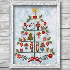 a cross - stitch christmas tree with presents on it in a white frame against a wooden wall