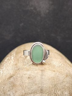 Sage green Puerto Rico seaglass and leaf ring. The green glass features a sterling silver leaf, round wire halo, and ball surrounding it. It sits atop a 4mm wide band, size 8.5. This style reminds me of art-deco, and I absolutely love it!  *Please take special care of your sea glass/gemstone jewelry! The glass (like any other glass, tumbled or not) can be cracked or broken if handled too rough. I use mainly sterling silver components for my pieces. Sterling silver does tarnish over time, and can Seaglass Rings, Handmade Green Rings With Recycled Glass, Gold Sea Glass Ring, Green Sea Glass Jewelry, Adjustable Sea Glass Ring Jewelry, Silver Recycled Glass Ring, Silver Sea Glass Ring For Beach, Leaf Ring, Art Deco Ring