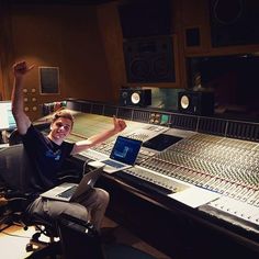 a man sitting in front of a mixing desk with his arms up and laptop on the table