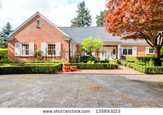 a large brick house with hedges and trees in the front yard on a sunny day