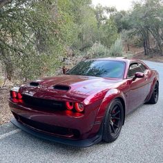 a red sports car is parked on the side of the road in front of some trees